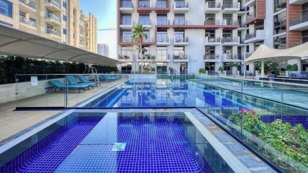 A rooftop swimming pool with glass railings, surrounded by modern apartment buildings. - Modern Balcony Studio in Arjan - Near Miracle Garden & Mall of the Emirates (Dubai)