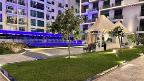 A modern hotel courtyard with a pool, outdoor seating, and a well-maintained lawn. - Modern Balcony Studio in Arjan - Near Miracle Garden & Mall of the Emirates (Dubai)