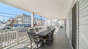 Ein überdachter Balkon mit Tisch und Stühlen, einem weißen Geländer und Blick auf die Straße und die Häuser.