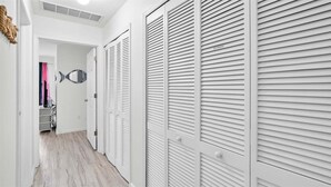 Un pasillo con armarios blancos, un espejo y una puerta que da a una habitación con cortina rosa.