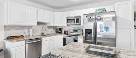 A modern kitchen with white cabinets, stainless steel appliances, and a marble countertop.