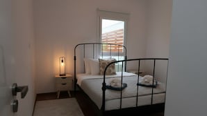 Ein Schlafzimmer mit einem Metallbettgestell, einem Nachttisch mit Lampe, einem Fenster mit Jalousien und einer weißen Tür.