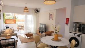 Ein modernes Wohnzimmer mit Essbereich, einer Küche und einem Waschraum. Es gibt einen Fernseher, eine Couch, einen Esstisch und Stühle.