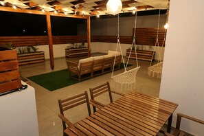 Een terras buiten met houten meubels, waaronder een tafel en stoelen, en hangstoelen.
