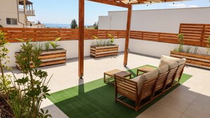 Eine Dachterrasse mit Holzmöbeln, Pflanzgefässen mit Grünpflanzen und Blick auf das Meer.