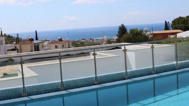 Ein klarer, blauer Pool mit Metallgeländern, Blick auf das Meer und Gebäude im Hintergrund.