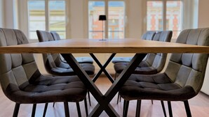 Una mesa de conferencias con cuatro sillas tapizadas, estructura de metal negro y grandes ventanales con vistas a edificios.