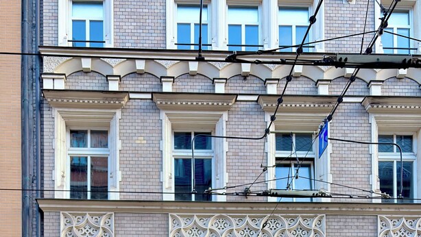 Un edificio con una entrada arqueada grande, un letrero con un símbolo de neón y un escaparate donde se ve a una persona en el interior.