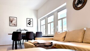 Una sala moderna con un sofá, un comedor con sillas y un gran ventanal.
