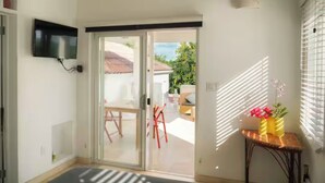 Una sala moderna con un televisor montado en la pared, un ventanal corredizo que da a un patio exterior y una pequeña mesa con un florero.