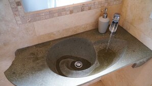 Un lavamanos de piedra con un grifo moderno y dispensador de jabón en un baño con azulejos color crema.
