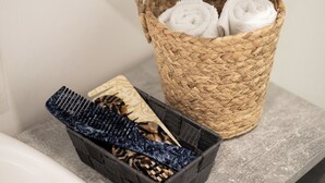 Une salle de bain avec un panier en osier contenant des serviettes enroulées et un plateau noir avec des articles de toilette.