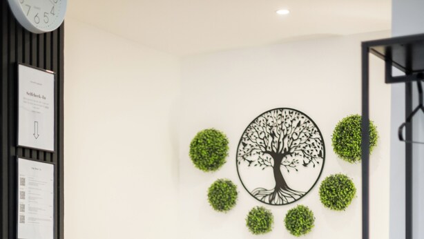 Une chambre à coucher moderne avec un lit, une horloge murale, un certificat encadré et un élément décoratif représentant un arbre sur le mur.