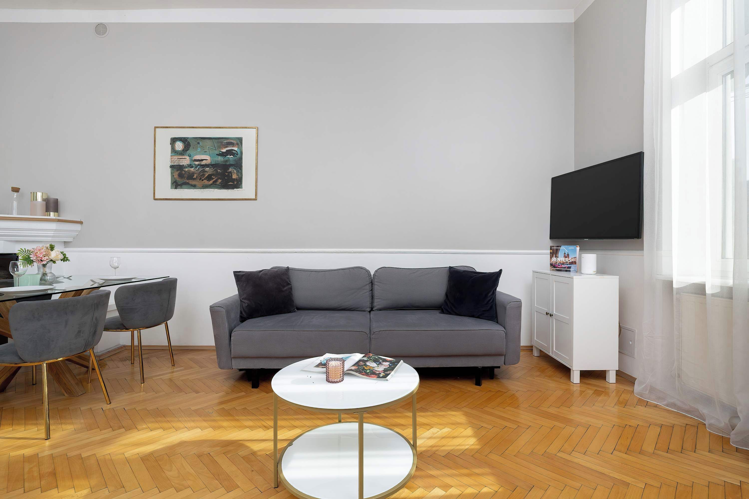 A modern living room with a grey sofa, a round coffee table, and a dining area with a white table and chairs.