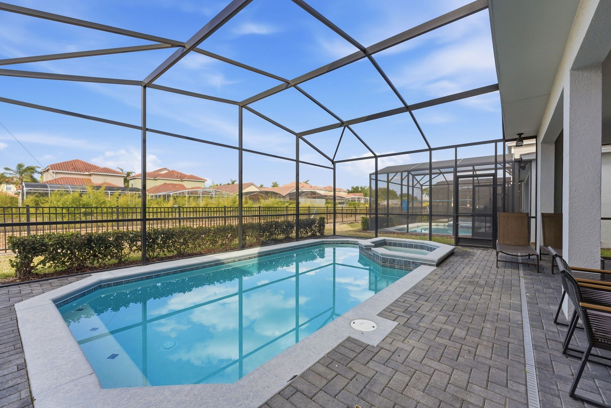 Une piscine dotée d’une structure en verre, entourée d’une terrasse en briques et de mobilier d’extérieur.