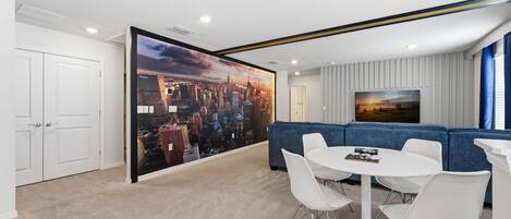 A modern room with a cityscape mural, a blue sofa, white chairs, and a small table.