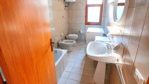 Pieni kylpyhuone, jossa on wc, bidee, kylpyamme ja pesuallas.