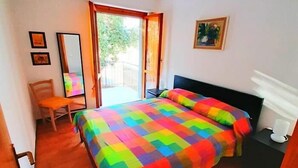 Makuuhuoneessa on sänky, tuoli, työpöytä, yöpöytä ja ikkuna, josta on näkymä vehreään maisemaan.