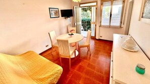 Una habitació amb un llit, una taula de dinar amb cadires, una televisió i una finestra amb vista a la vegetació.