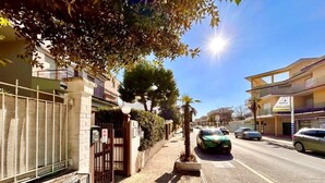 Vista d'un carrer amb una entrada tancada per reixa, una palmera i un edifici amb un rètol que diu 'Arbuatti'.