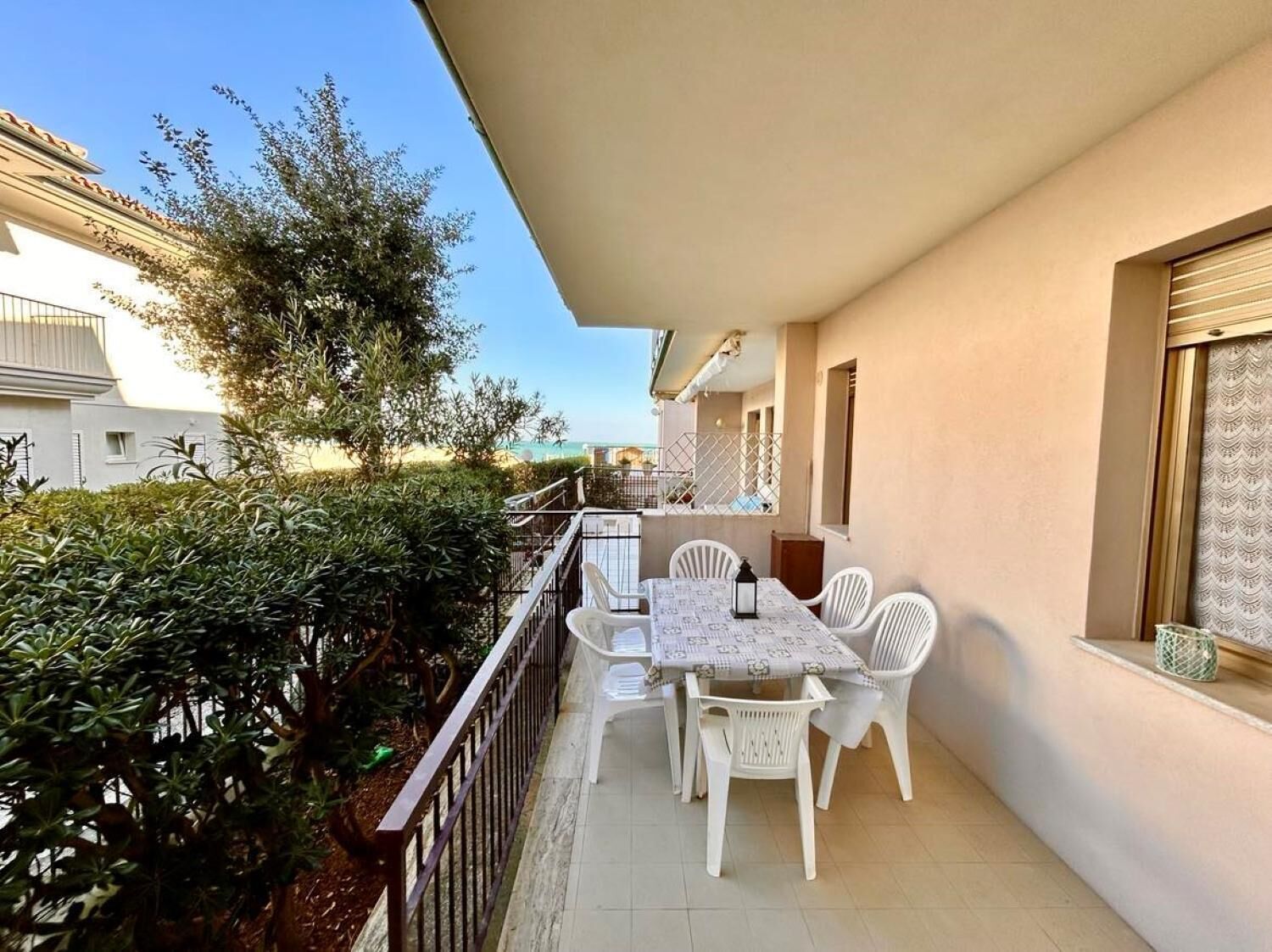 A balcony with a table and chairs, surrounded by greenery and a view of the sea.
