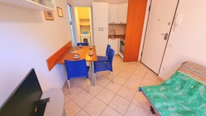 A compact room with a dining table, two chairs, a TV, a bed with a patterned bedspread, and a kitchenette with a washing machine. - Two-room Caesar [center, park, terrace] (Sirolo)