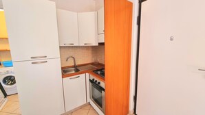 A compact kitchen with white cabinets, a sink, a stove, and a washing machine in the corner. - Two-room Caesar [center, park, terrace] (Sirolo)