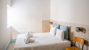 Een hotelkamer met een bed, een stoel, een plafondventilator en een raam dat natuurlijk licht binnenlaat.