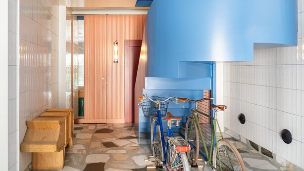 Een gang met betegelde muren, een houten bank en fietsen.
