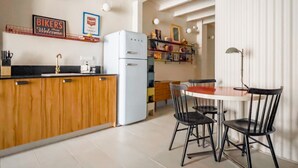 Een keuken met houten kasten, een witte koelkast, en een eethoek met twee zwarte stoelen en een tafel.