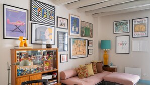 Een gezellige woonkamer met een bank, een bijzettafeltje, een boekenkast en diverse ingelijste kunstwerken aan de muren.