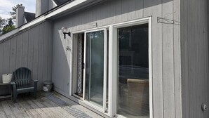 A building with a sliding glass door, a chair, and a small table on the deck. - Tenney Mountain Ski Resort Condo (Plymouth)