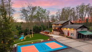 A two-story stone house with a tennis court, surrounded by trees and a clear sky. - Luxury meets Wilderness in the Heart of Poconos (Albrightsville)