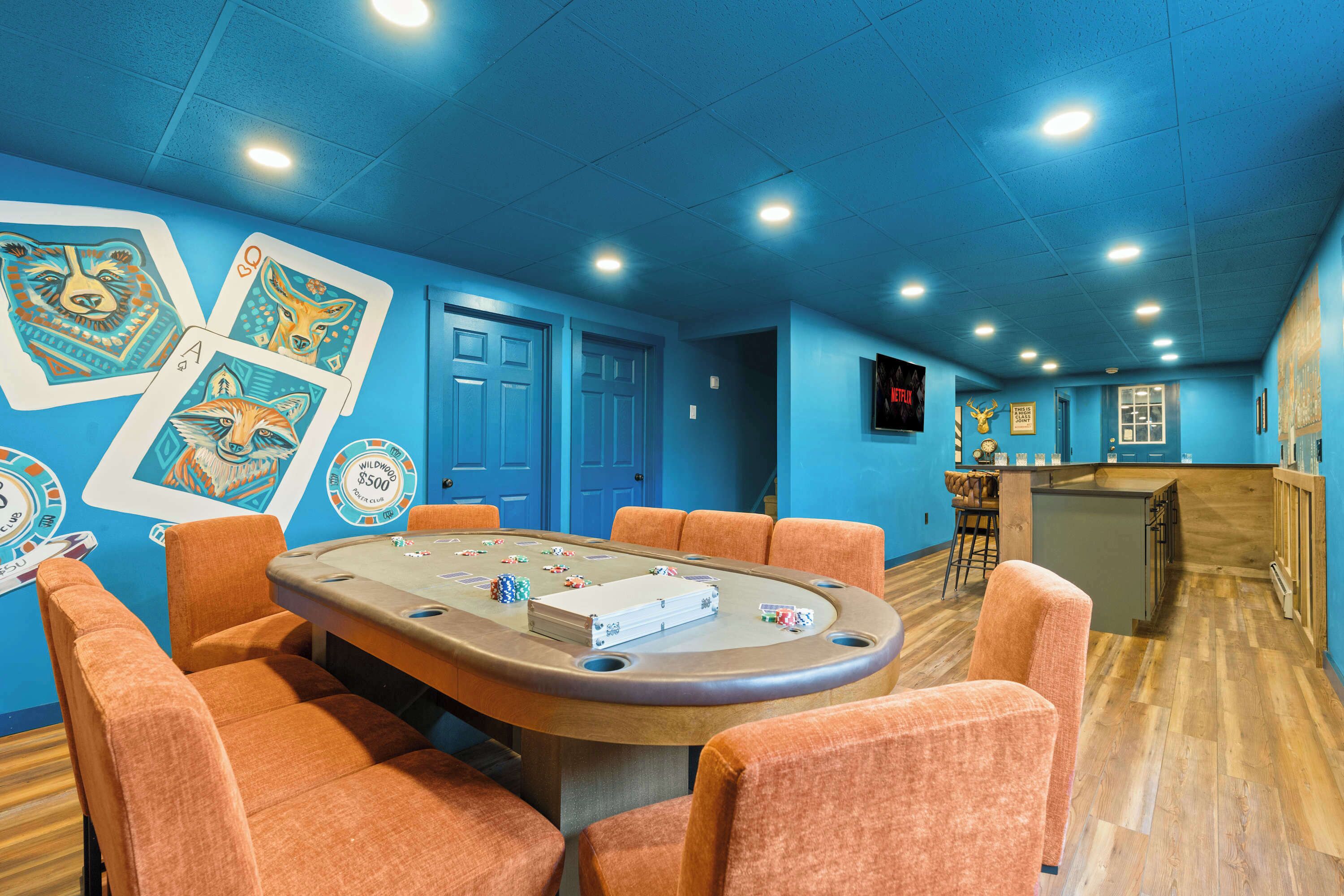 A casino room with a poker table, orange chairs, and blue walls with playing cards.
