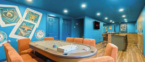 A casino room with a poker table, orange chairs, and blue walls with playing cards.