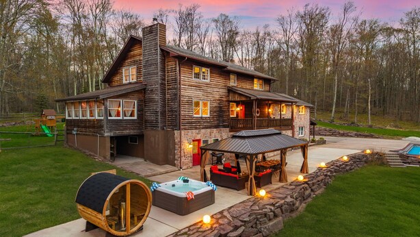 A log cabin with a hot tub, outdoor seating, and a stone wall. - Luxury meets Wilderness in the Heart of Poconos (Albrightsville)