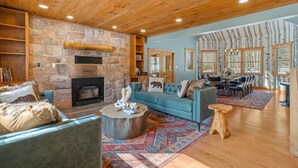 A cozy living room with a stone fireplace, blue sofa, and wooden ceiling. - Luxury meets Wilderness in the Heart of Poconos (Albrightsville)