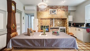 A dining area with a table set for two, a wooden clock, and a fireplace. - Renovated Country House in a Charming Hamlet (Ligneyrac)