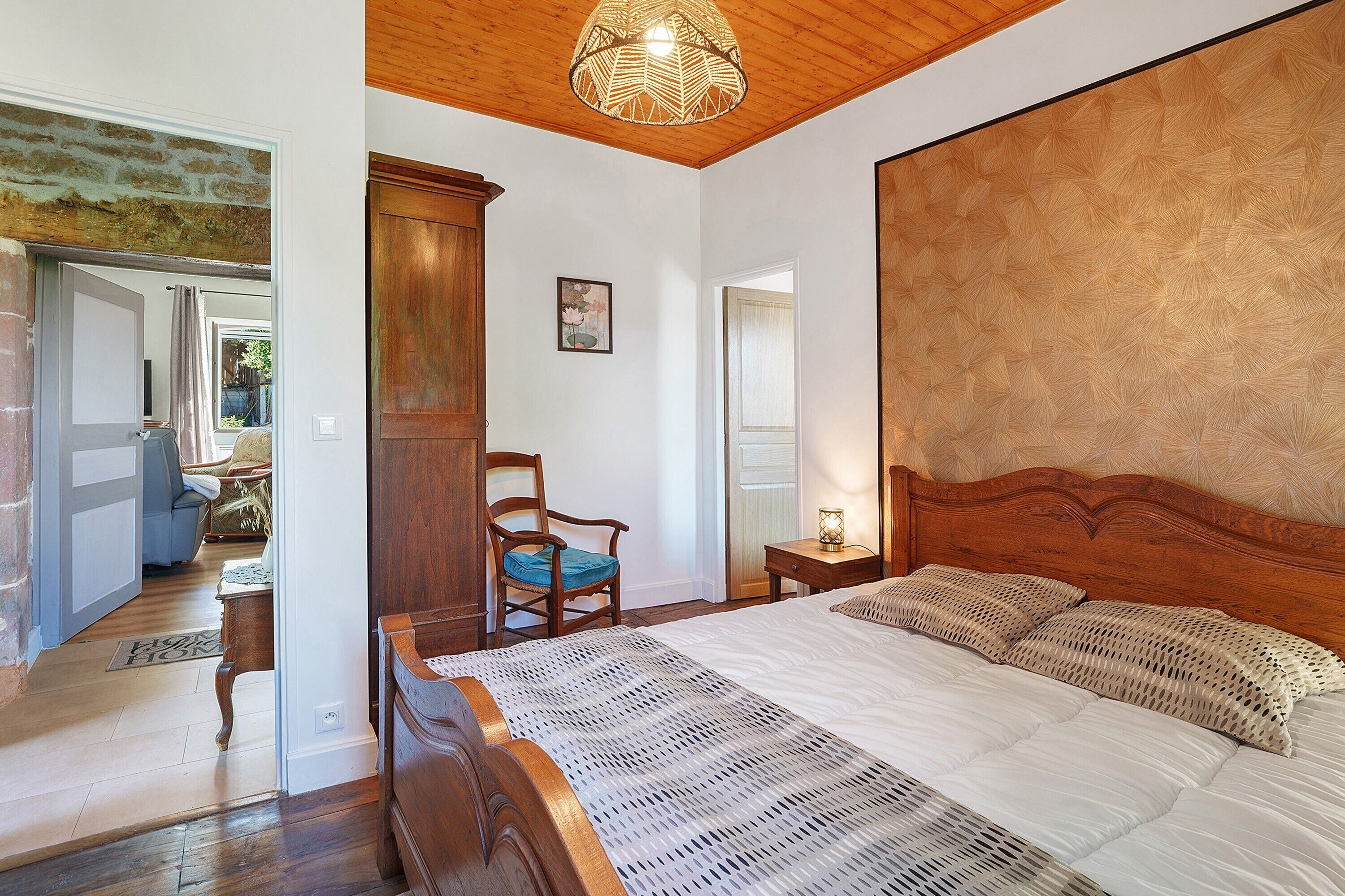 A bedroom with a wooden headboard, a bed with white bedding, a wooden nightstand, a chair, and a wooden cabinet.