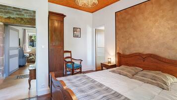 A bedroom with a wooden headboard, a bed with white bedding, a wooden nightstand, a chair, and a wooden cabinet.