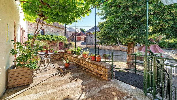 A covered outdoor area with stone steps, potted plants, a table, and a metal gate. - Renovated Country House in a Charming Hamlet (Ligneyrac)