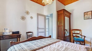 A bedroom with a bed, a desk, a chair, a wardrobe, and a door leading to another room. - Renovated Country House in a Charming Hamlet (Ligneyrac)