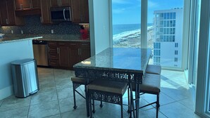 Una cocina con armarios de madera, un refrigerador de acero inoxidable y un amplio ventanal con vista a la playa.