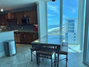 A kitchen with wooden cabinets, a stainless steel refrigerator, and a large window overlooking the beach. - Bel Solé 1801 Penthouse 4 bedroom 4 bath located directly on Little Lagoon. (Gulf Shores)