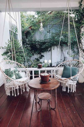 A wooden deck with two white wicker chairs and a small round table, surrounded by lush greenery. - Cozy Family & Friends Retreat With Lush Garden (Gili Trawangan)