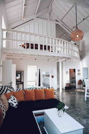A spacious loft with a high ceiling, a curved staircase, and a large black and orange sofa. - Cozy Family & Friends Retreat With Lush Garden (Gili Trawangan)