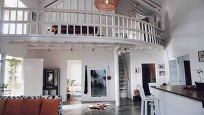 A spacious loft with a high ceiling, a mezzanine level, and a central staircase. - Cozy Family & Friends Retreat With Lush Garden (Gili Trawangan)