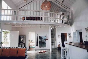A spacious loft with a high ceiling, a mezzanine level, and a central staircase. - Cozy Family & Friends Retreat With Lush Garden (Gili Trawangan)