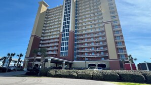 Un hotel de varios pisos con un atrio central, balcones en cada planta y un estacionamiento con varios automóviles.