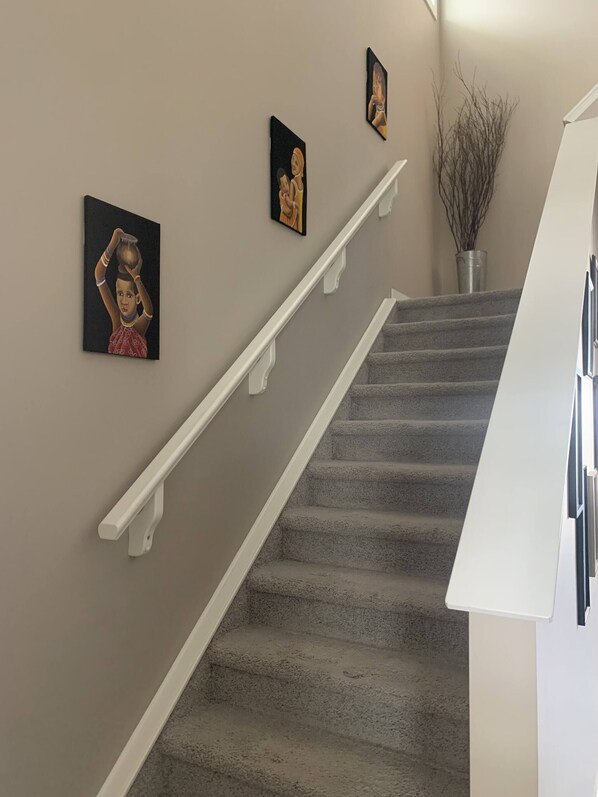 A staircase with a white handrail and beige walls. There are three framed artworks on the wall.